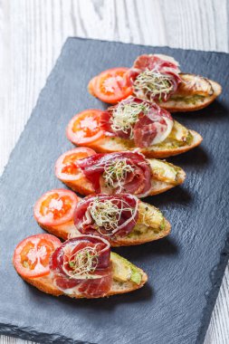 Meze bruschetta salam, domates, kabak ciabatta ekmeği taş arduvaz arka plan üzerinde tarih ile kapatın. Lezzetli aperatifler, sandviçler, crostini, parti ya da piknik zamanında antipasti. Üstten Görünüm