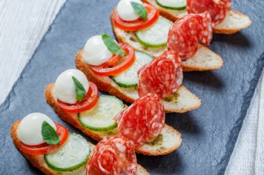Caprese sandviç domates, mozzarella peyniri, fesleğen, salam taş arduvaz arka plan üzerinde ciabatta ekmeği üzerine kapatın. Lezzetli meze aperatifler, bruschetta, crostini, antipasti. Üstten Görünüm