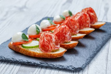 Caprese sandviç domates, mozzarella peyniri, fesleğen, salam taş arduvaz arka plan üzerinde ciabatta ekmeği üzerine kapatın. Lezzetli meze aperatifler, bruschetta, crostini, antipasti. Üstten Görünüm