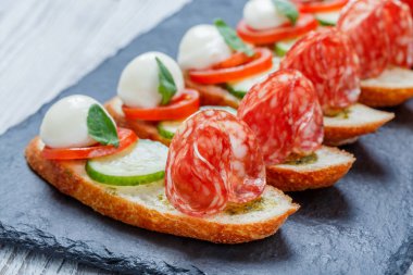 Caprese sandviç domates, mozzarella peyniri, fesleğen, salam taş arduvaz arka plan üzerinde ciabatta ekmeği üzerine kapatın. Lezzetli meze aperatifler, bruschetta, crostini, antipasti. Üstten Görünüm