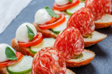 Caprese sandviç domates, mozzarella peyniri, fesleğen, salam taş arduvaz arka plan üzerinde ciabatta ekmeği üzerine kapatın. Lezzetli meze aperatifler, bruschetta, crostini, antipasti. Üstten Görünüm