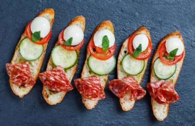 Caprese sandviç domates, mozzarella peyniri, fesleğen, salam taş arduvaz arka plan üzerinde ciabatta ekmeği üzerine kapatın. Lezzetli meze aperatifler, bruschetta, crostini, antipasti. Üstten Görünüm