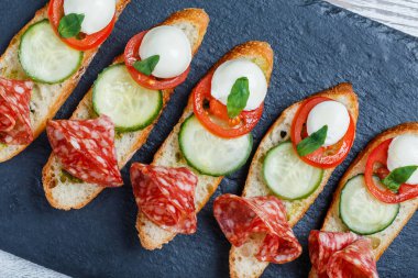 Caprese sandviç domates, mozzarella peyniri, fesleğen, salam taş arduvaz arka plan üzerinde ciabatta ekmeği üzerine kapatın. Lezzetli meze aperatifler, bruschetta, crostini, antipasti. Üstten Görünüm