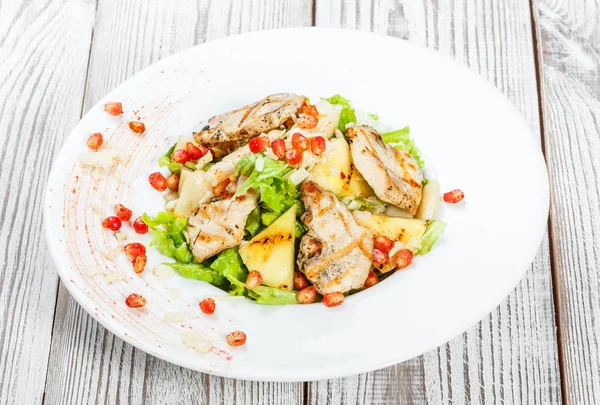 Tavuk göğsü, kavun, ananas, nar taneleri ile taze salata, marul yaprakları ve badem ahşap arka plan üzerinde plaka üzerinde yakın çekim. Üstten Görünüm