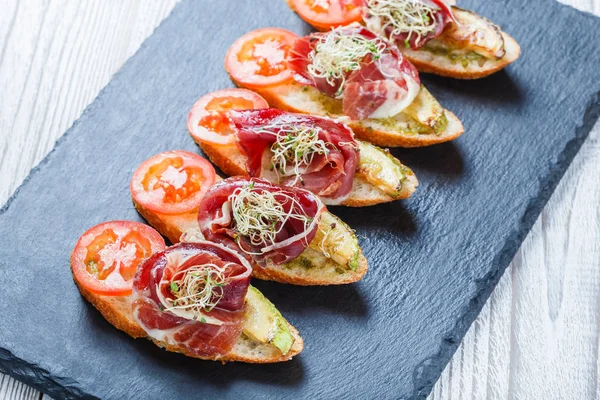 Meze bruschetta salam, domates, kabak ciabatta ekmeği taş arduvaz arka plan üzerinde tarih ile kapatın. Lezzetli aperatifler, sandviçler, crostini, parti ya da piknik zamanında antipasti. Üstten Görünüm