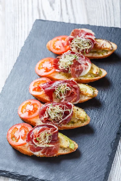 Meze bruschetta salam, domates, kabak ciabatta ekmeği taş arduvaz arka plan üzerinde tarih ile kapatın. Lezzetli aperatifler, sandviçler, crostini, parti ya da piknik zamanında antipasti. Üstten Görünüm