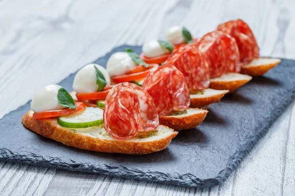 Caprese sandviç domates, mozzarella peyniri, fesleğen, salam taş arduvaz arka plan üzerinde ciabatta ekmeği üzerine kapatın. Lezzetli meze aperatifler, bruschetta, crostini, antipasti. Üstten Görünüm