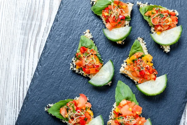 Appetizer canape with chopped vegetables and sesame on stone slate background close up. Delicious snacks, sandwiches, crostini, bruschetta, antipasti on party or picnic time. Top view