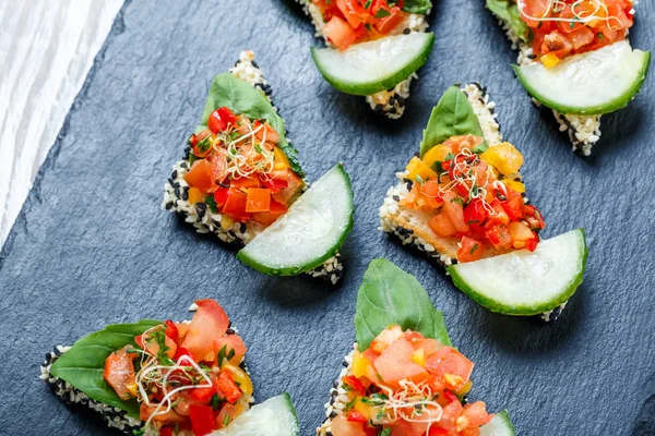 Appetizer canape with chopped vegetables and sesame on stone slate background close up. Delicious snacks, sandwiches, crostini, bruschetta, antipasti on party or picnic time. Top view