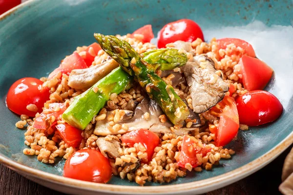 Здоровый салат из ячменной каши со спаржей, помидорами и грибами на тарелке. Веганская еда — стоковое фото