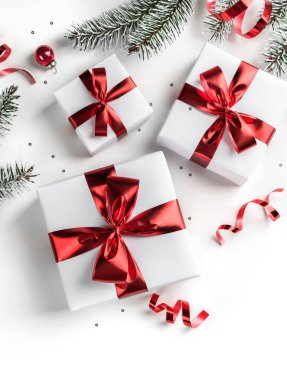 Noel ağacı dalları, kırmızı kurdeleli hediye kutuları, kırmızı süslemeler, parıltılar ve beyaz arka planda konfeti. Noel ve yeni yıl tebrik kartı, kış tatili. Düz yatış, üst görünüm