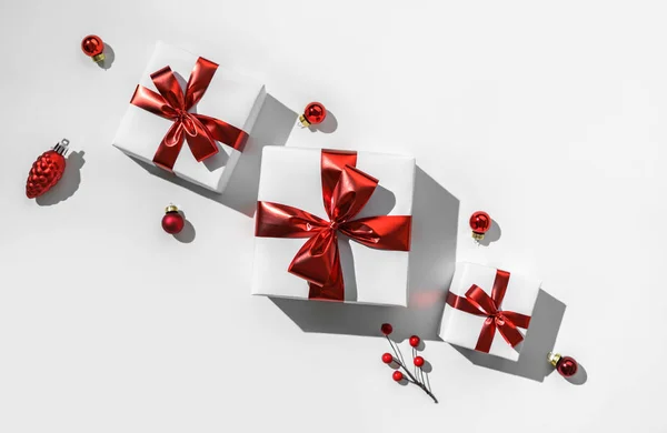 Χριστουγεννιάτικα κουτιά δώρου με κόκκινη κορδέλα και διακόσμηση σε λευκό φόντο. Xmas και καλές πρωτοχρονιάτικες διακοπές, bokeh, φως. Επίπεδο lay, κορυφαία άποψη, σκληρή σκιά — Φωτογραφία Αρχείου