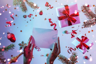Noel Baba 'ya renkli parlak mavi ve mor arka plan, uçan Noel süsleri, hediye kutuları, parıltılar ve konfetilerle ilgili bir mektup tutan kadın eller. Xmas ve yeni yıl tatili, bokeh, ışık