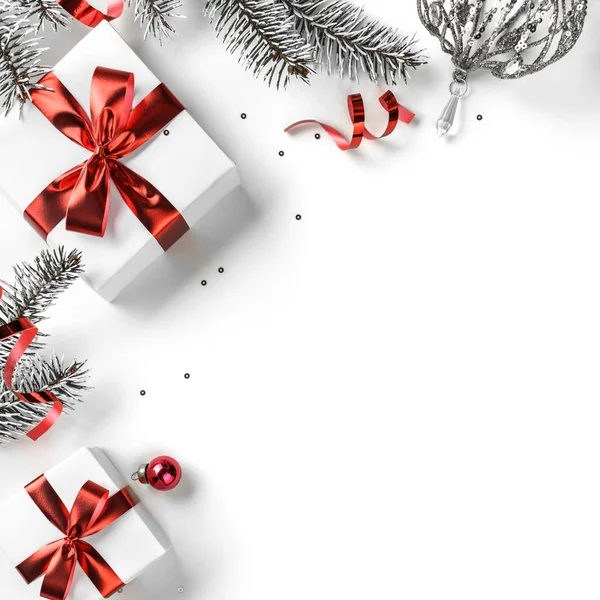 Noel ağacı dalları, kırmızı kurdeleli hediye kutuları, kırmızı süslemeler, parıltılar ve beyaz arka planda konfeti. Noel ve yeni yıl tebrik kartı, kış tatili. Düz yatış, üst görünüm