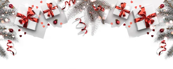 Noel ağacı dalları, kırmızı kurdeleli hediye kutuları, kırmızı süslemeler, parıltılar ve beyaz arka planda konfeti. Noel ve yeni yıl tebrik kartı, kış tatili. Düz yatış, üst görünüm