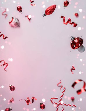 Uçan süslemelerden, kırmızı dekordan, toplardan, pırıltılardan ve açık pembe arka planda konfetiden oluşan mutlu Noeller kartı. Noel ve Yeni Yıl tatili, Bokeh, ışık. Seçici odak