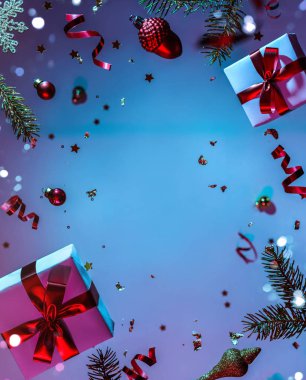 Mutlu Noeller ve yeni yıl geçmişi. Uçan süslemelerden yapılmış Noel kartı, köknar dalları, toplar, kar taneleri, ışıltılar, hediye kutuları, renkli neon mavi ve mor arka planda bokeh