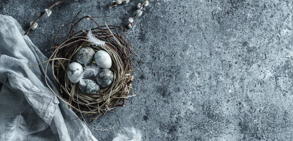 Marble Easter eggs in bird nest with feathers and spring flowers on blue background with napkin. Happy Easter holiday, top view, flat lay, wide composition — Stock Photo, Image