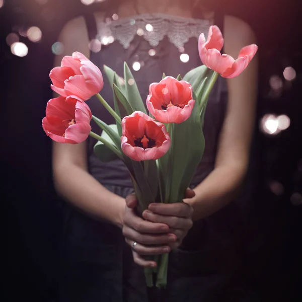 Vrouw handen houden roze tulpen bloemen op donkere achtergrond met licht, bokeh. Fijne paasvakantie, Valentijnsdag, Vrouw Dag, selectieve focus — Stockfoto