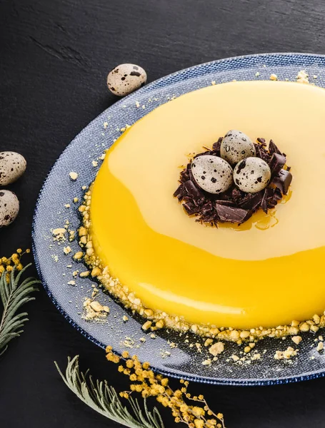 Easter cake with yellow mirror glaze, chocolate, spring flowers, quail eggs on dark stone background. Happy Easter celebration. Top view — Stock Photo, Image