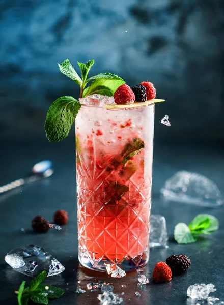 Cóctel de bayas frescas con frambuesa, mora, menta y hielo en vaso de frasco sobre fondo azul oscuro. Un trago en cámara congelada, volando hielo. Bebida fría de verano y cóctel — Foto de Stock