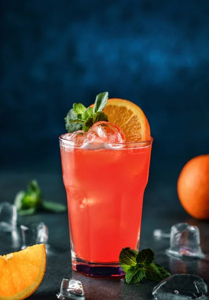 Cóctel tropical fresco con naranja, menta y hielo en vaso sobre fondo azul oscuro. Bebida fría de verano y cóctel — Foto de Stock