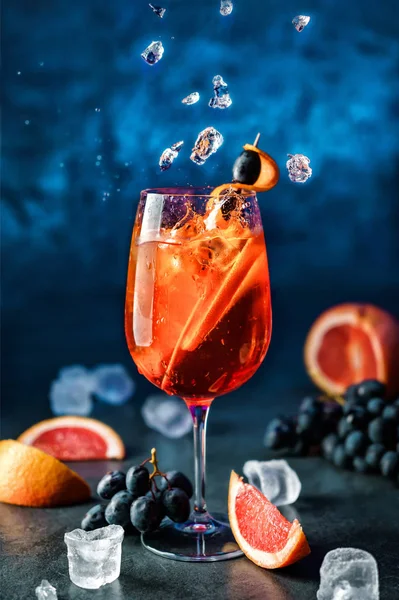 Cocktail de toranja fresco com laranja, uvas e gelo em vinho sobre fundo azul escuro. Estúdio tiro de bebida em movimento de congelamento, gelo voador, gotas em respingo líquido. Bebida fria de verão e coquetel — Fotografia de Stock