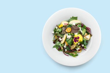 Sağlıklı taze salata ile karışık yeşiller, elma, krem peynir, kızılcık, sos ve mavi arka planda izole edilmiş yenilebilir çiçekler. Sağlıklı yiyecekler, vejetaryen diyeti, üst manzara.