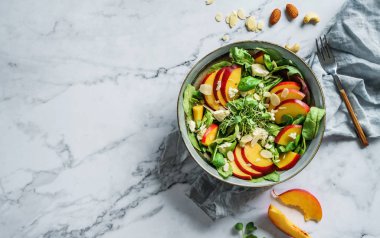 Şeftalili taze yaz salatası, ıspanak, mikro yeşiller, açık mermer arka planda beyaz peynir ve badem. Sağlıklı yemek, temiz yemek, Buda kasesi salatası, üst manzara.