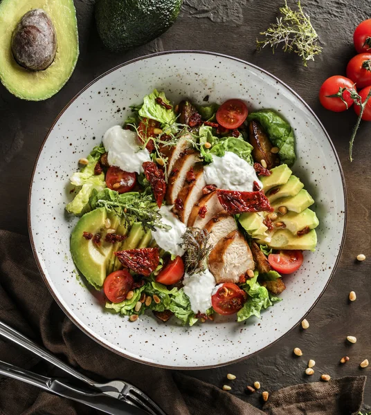 Ensalada saludable con filete de pollo, aguacate, tomates, lechuga, verduras, piñones y salsa en tazón sobre fondo de madera. Comida saludable, alimentación limpia, dieta, tazón de buda, vista superior — Foto de Stock