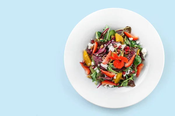 Gesunder frischer Salat mit Mischgemüse, Erdbeere, Orange, Nüssen, Frischkäse und essbaren Blumen in einem Teller auf blauem Hintergrund. gesunde Ernährung, vegetarische Ernährung, Draufsicht — Stockfoto