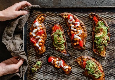 Elleri fırında patates kızartması, nohut, domates, keçi peyniri soslu guacamole, avokado, kahverengi arka planda fidanlar. Sağlıklı vejetaryen yemekleri, temiz yemek, üst manzara.