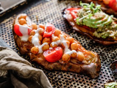 Kızarmış bezelye, domates, keçi peyniri soslu guacamole, avokado, kahverengi arka planda pişirme tepsisindeki tohumlarla fırında patates tostu. Sağlıklı vejetaryen yemekleri, temiz yemek, diyet, yakın çekim.