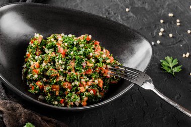 Bulgurlu Tabbouleh salatası, domates, maydanoz, yeşil soğan, siyah taş kaplama tabakta dolmalık biber. Geleneksel Ortadoğu ya da Arap yemeği. Sağlıklı yemek, vejetaryen diyeti, yakın çekim.