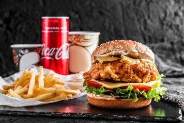MOLDOVA, KISHINEV - 27 Kasım 2018: Peynirli tavuk burger, domates, marul, sos ve konserve kola, siyah arkaplanda patates kızartması, öğle yemeği, yakın plan