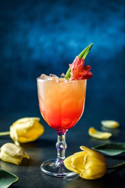 Buzlu taze tropikal kokteyl ve koyu mavi arka planda şarap kadehinde çiçekler. Soğuk yaz içeceği ve kokteyl