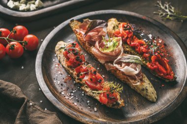 Prosciutto, domates, parmesan peyniri, sos pesto, ciabatta üzerine ızgara biber ve ahşap tabakta siyah arka planda çeşitli bruschetta çeşitleri. Sandviç seti şarap, üst manzara.