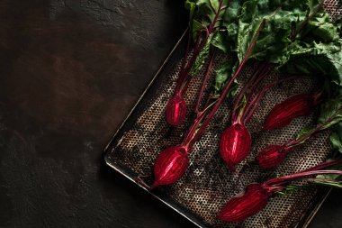 Koyu arkaplanda pişirme tepsisinde kızarmak için pancar. Taze sebzeler, sağlıklı organik yiyecekler, hasat, tarım, üst düzey görüş.