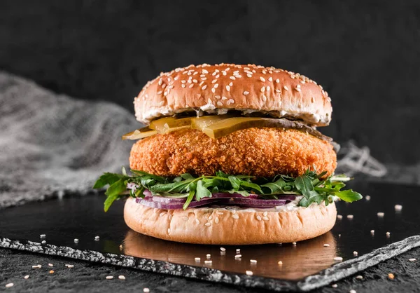 Turşulu tavuk burger, roka ve siyah arka planda sos.