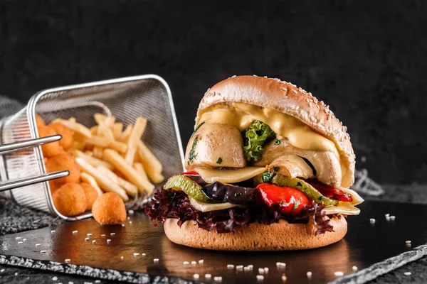 Vegetarian burger with cheese, zucchini, tomatoes, lettuce, mushrooms and fried stick balls, french fries on slate black background, close up