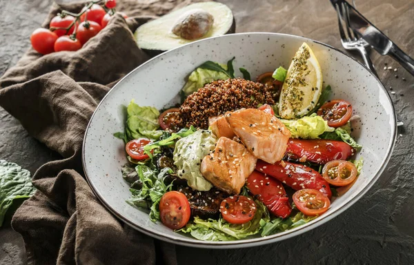 Healthy salad with fillet salmon, quinoa, avocado sauce, grilled pepper, tomatoes, lettuce, arugula in plate on wooden background. Healthy food, clean eating, Buddha bowl, dieting, close up