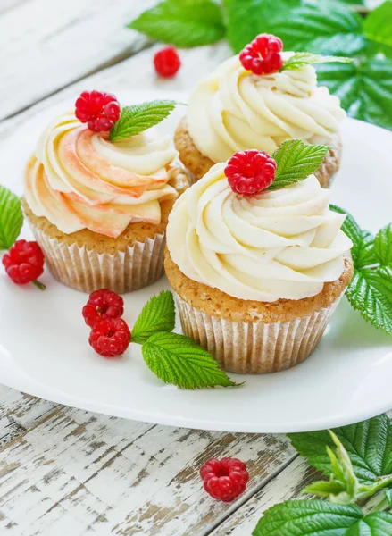 Delicados cupcakes de vainilla con crema y frambuesas sobre un fondo de madera blanca — Foto de Stock