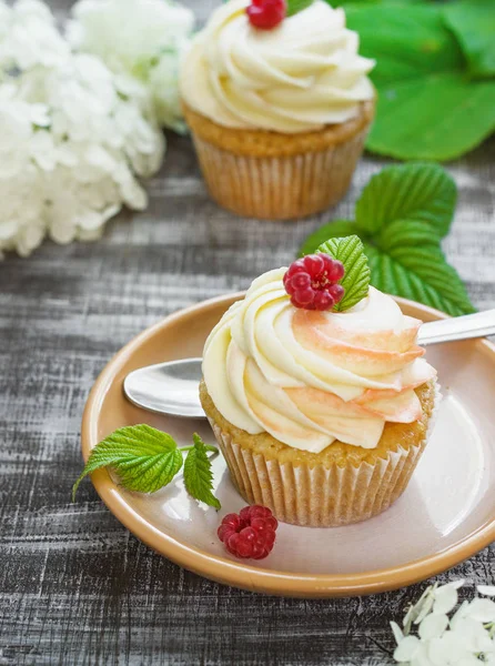 Jemné vanilkové cupcakes se smetanou a malinami na tmavém pozadí dřevěná — Stock fotografie