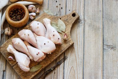 Ahşap bir tahta üzerinde çiğ tavuk bacağı ve yemek pişirmek için baharatlar.