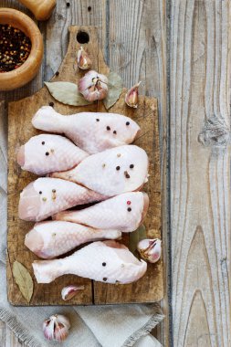 Ahşap bir tahta üzerinde çiğ tavuk bacağı ve yemek pişirmek için baharatlar.