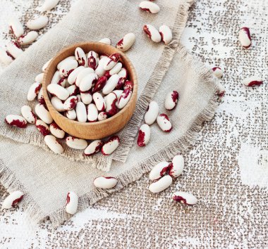 Açık arkaplanda, tahta bir fincanda beyaz-pembe fasulyeler.