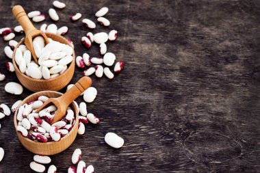 Koyu ahşap bir arka planda, ahşap bardaklarda renkli fasulyeler.