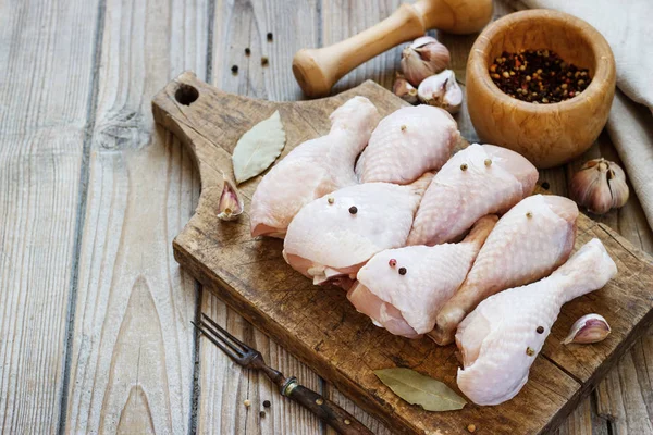 Ahşap bir tahta üzerinde çiğ tavuk bacağı ve yemek pişirmek için baharatlar.