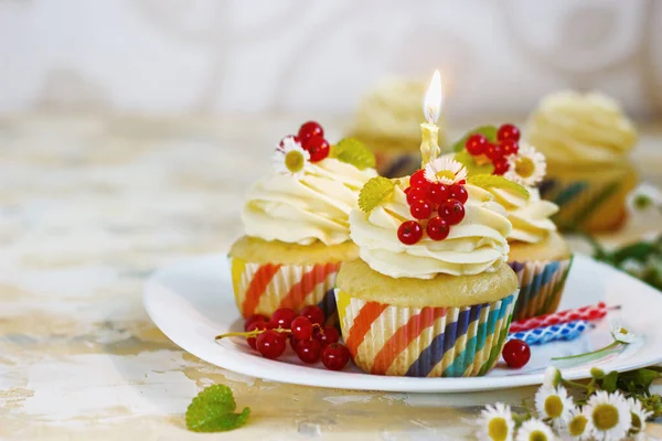 Skonsam, festlig cupcake med grädde och bär och ett ljus en ljus bakgrund — Stockfoto