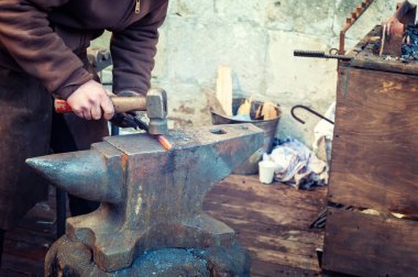 Demirci demir ocağında çekiçle çalışan bir demirci.